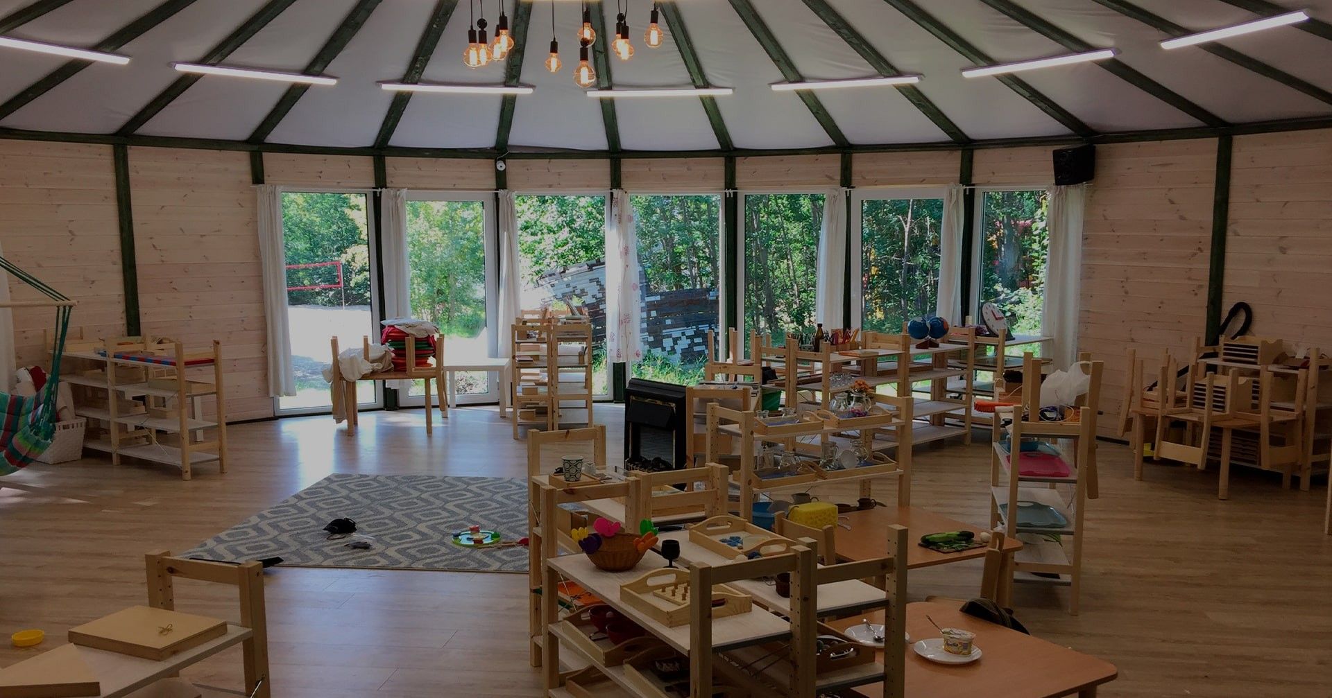 Wnętrze jurty: półki z pomocami Montessori i duże okna z widokiem na las
